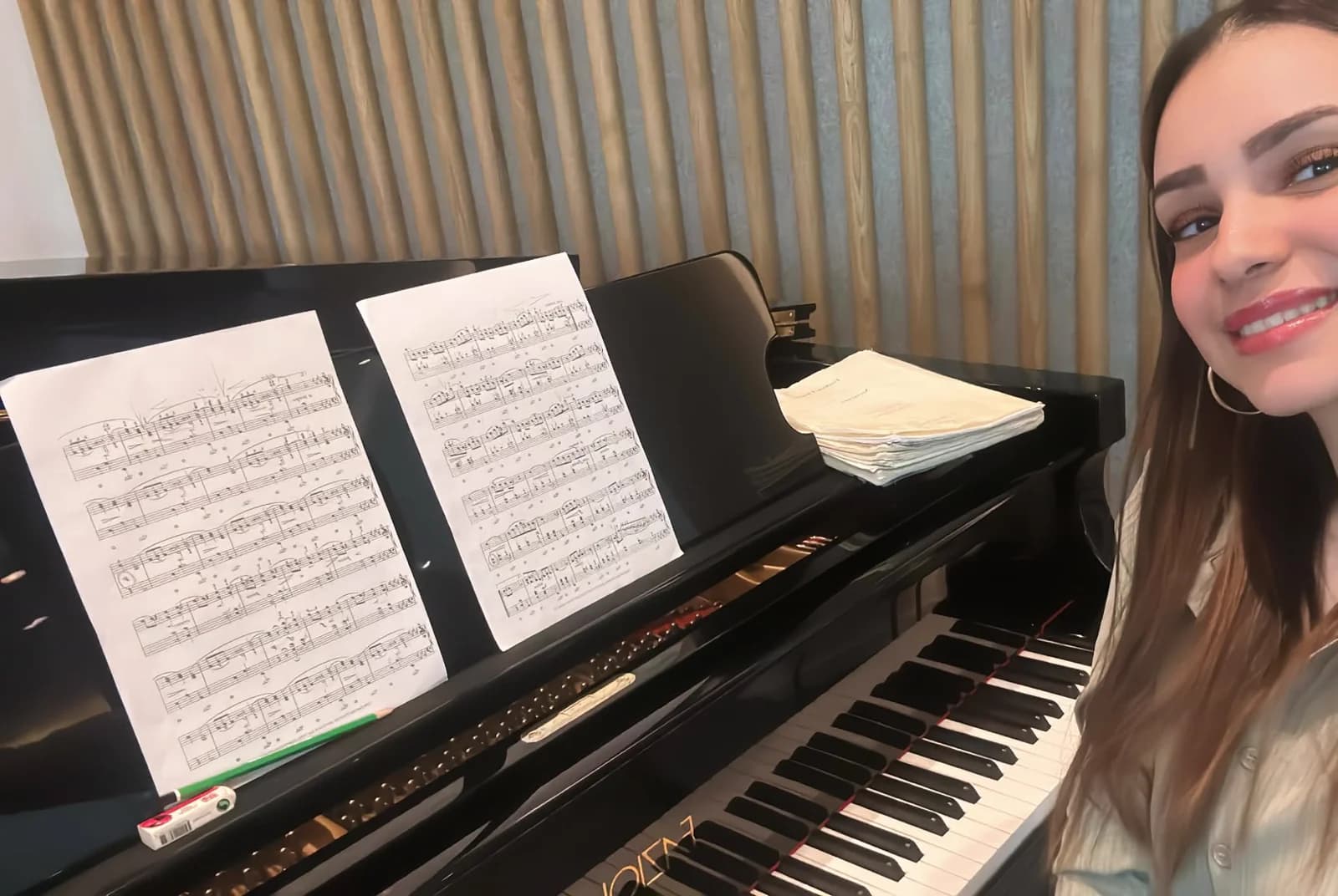 Inès sourit à côté de partitions posées sur le pupitre d’un piano à queue