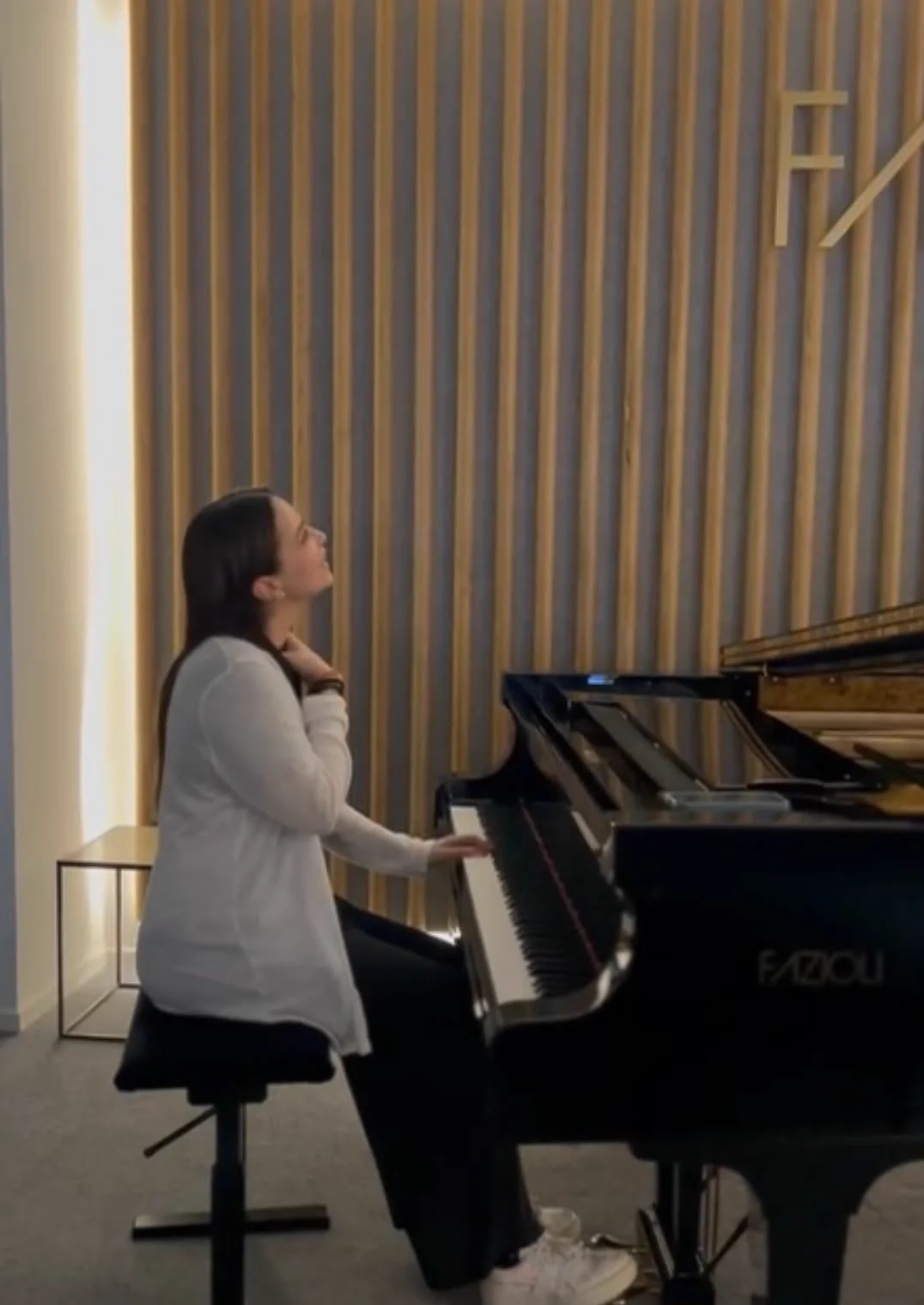 Inès au piano à queue dans une salle aux murs de bois, le regard levé