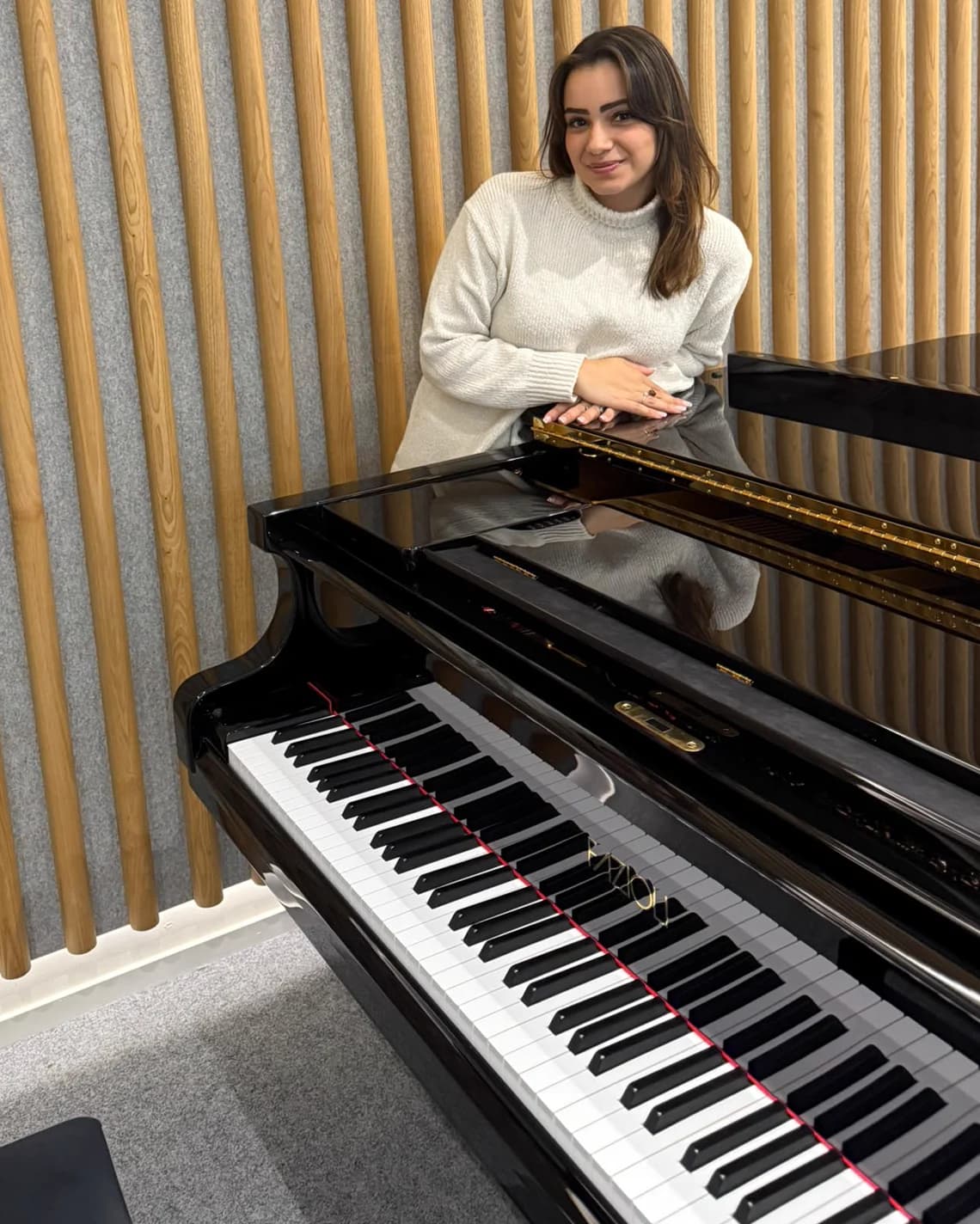 Inès, professeure de piano, accoudée à un piano à queue noir laqué